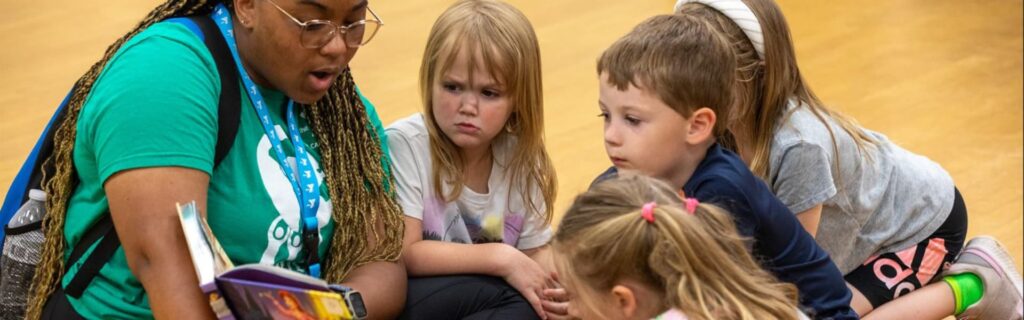 A teacher and kids reading a book in a gym