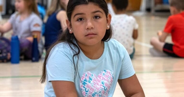 A child looking at the camera sitting in a gym