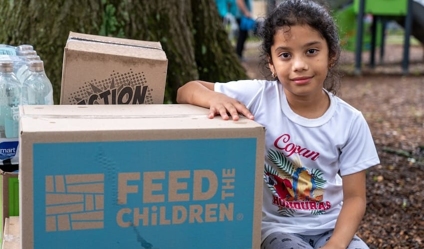 A girl with her arm on Feed the Children boxes outdoors
