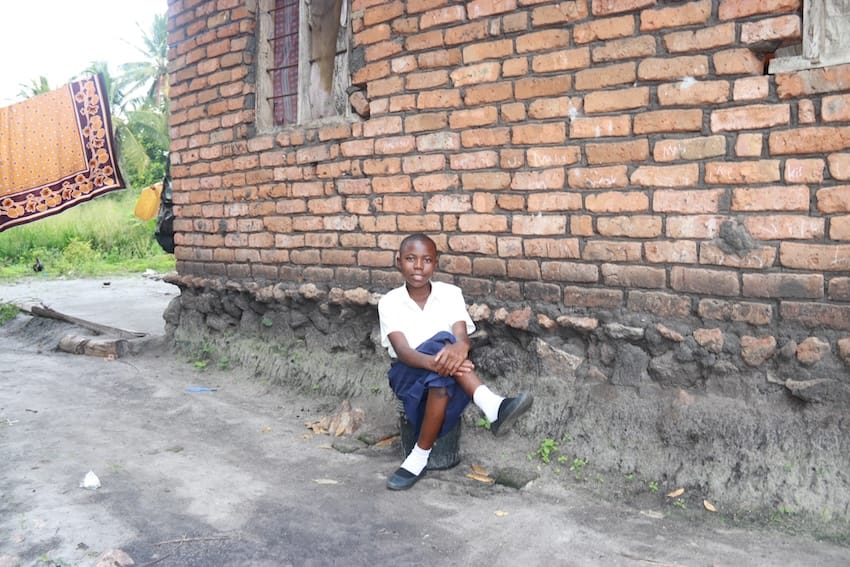 A child sitting on the concrete smiling outside of a house