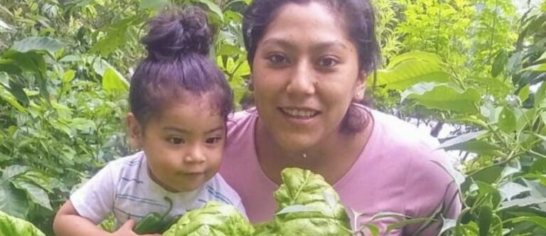 A mother and daughter outdoors surrounded by plants