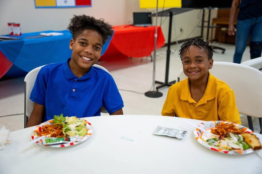 Two children smiling sitting at a table with food