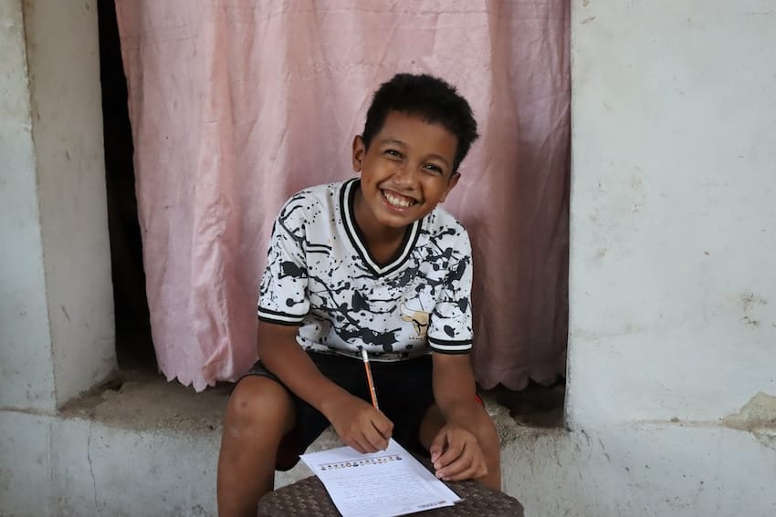 A boy smiling while writing on paper