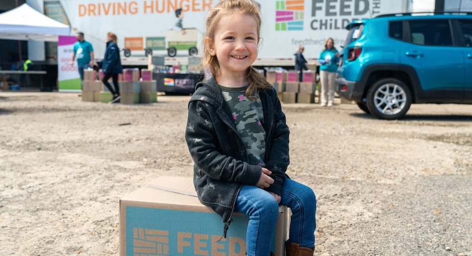 A child sitting on a box smiling at an outdoor event