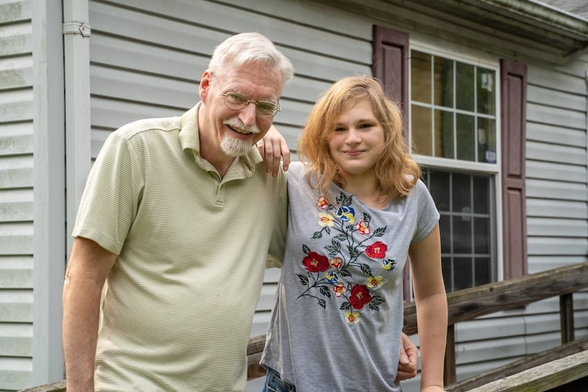 Mac and a child standing together outside a house