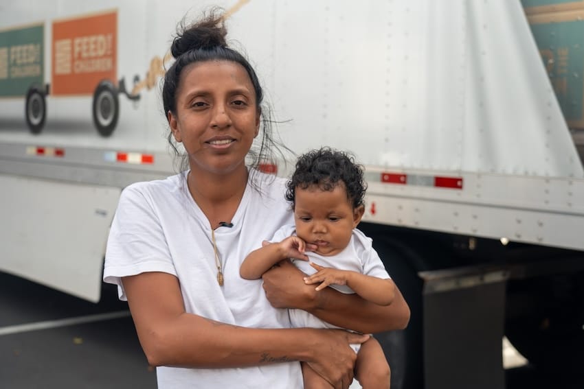 A mother holding her baby in front of a truck outdoors