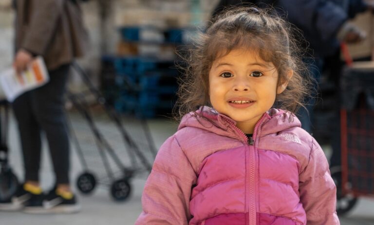 A child in a pink jacket at an outdoor event