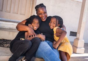 A woman and her children hugging on a house porch