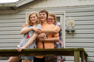 A small family hugging on the front porch of a house