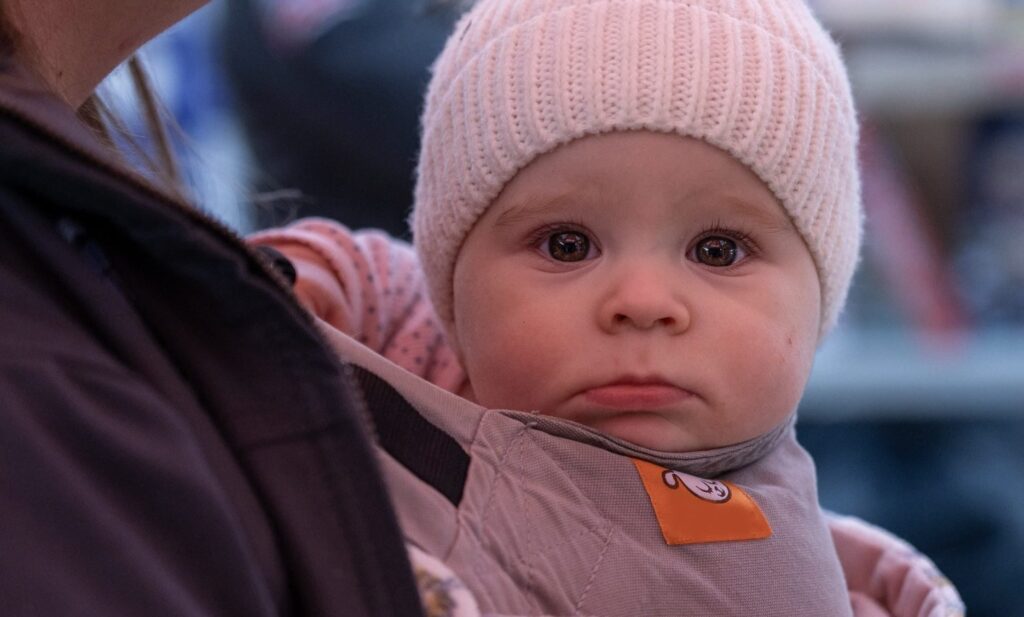 A baby being held by an adult in a pink hat