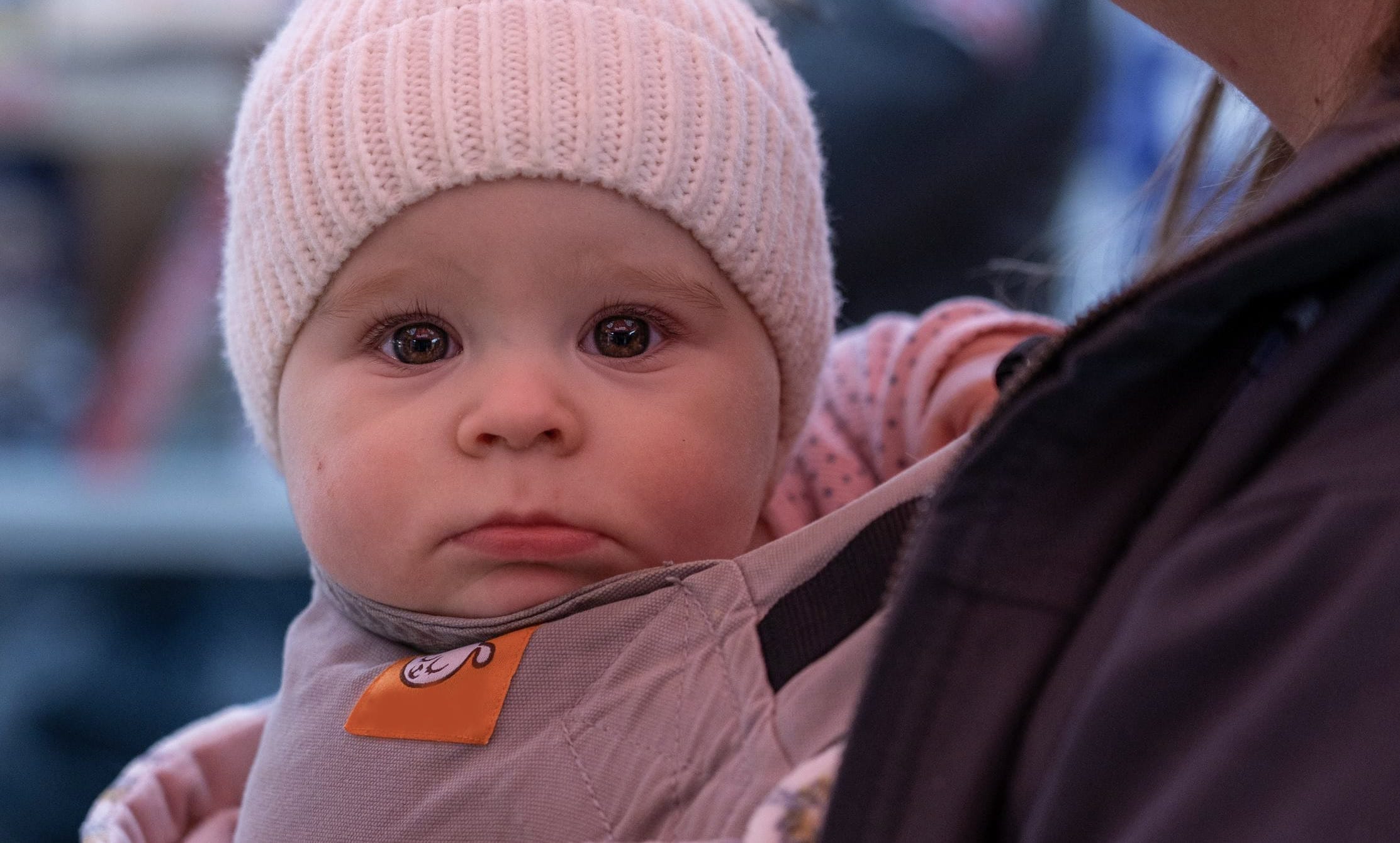 A baby being held by an adult in a pink hat